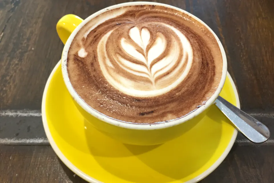 A cappuccino with latte art in a yellow cup and saucer