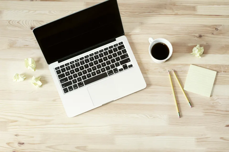 A laptop, notebook and coffee on a wooden desk